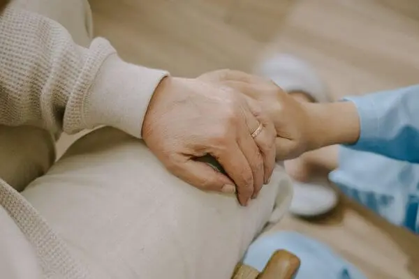 Das Bild des Pflegeteam Seifert zeigt zwei Hände. Die eine Hand ist die Hand eines alten Menschen, welche von der Hand einer Pflegekraft im Kassak gehalten wird.