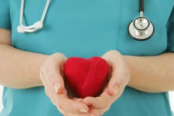 Das Bild des Pflegeteam Seifert für die Pflegeberatung zeigt den Oberkörper einer Pflegekraft in einem Kassak, welche in Ihren Händen ein rotes Herz aus Filz trägt.
